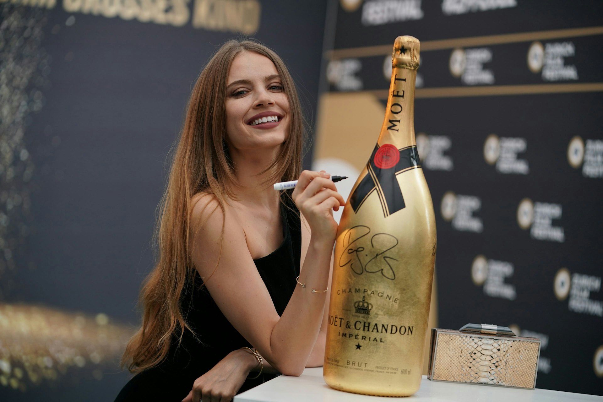 A woman signs a big gold Moët bottle.
