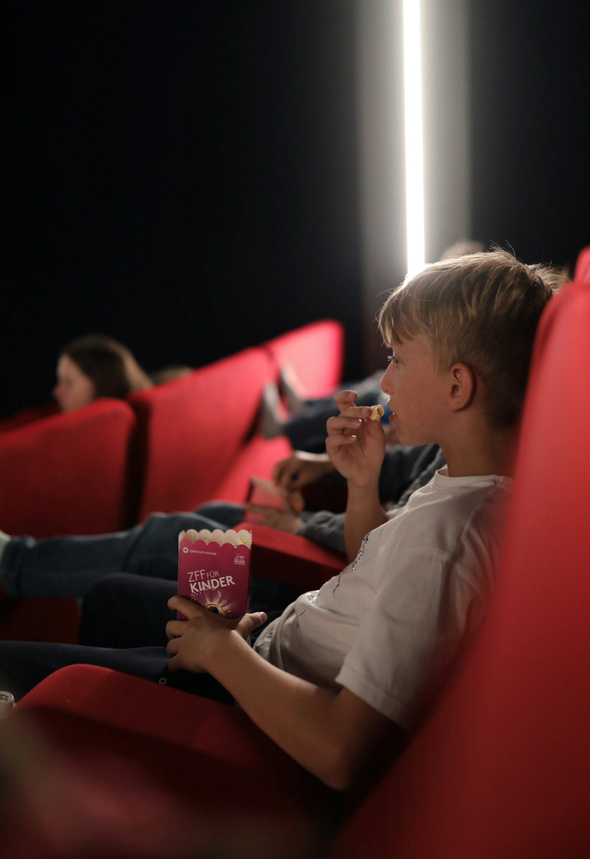 Children in a cinema auditorium. They are eating popcorns.